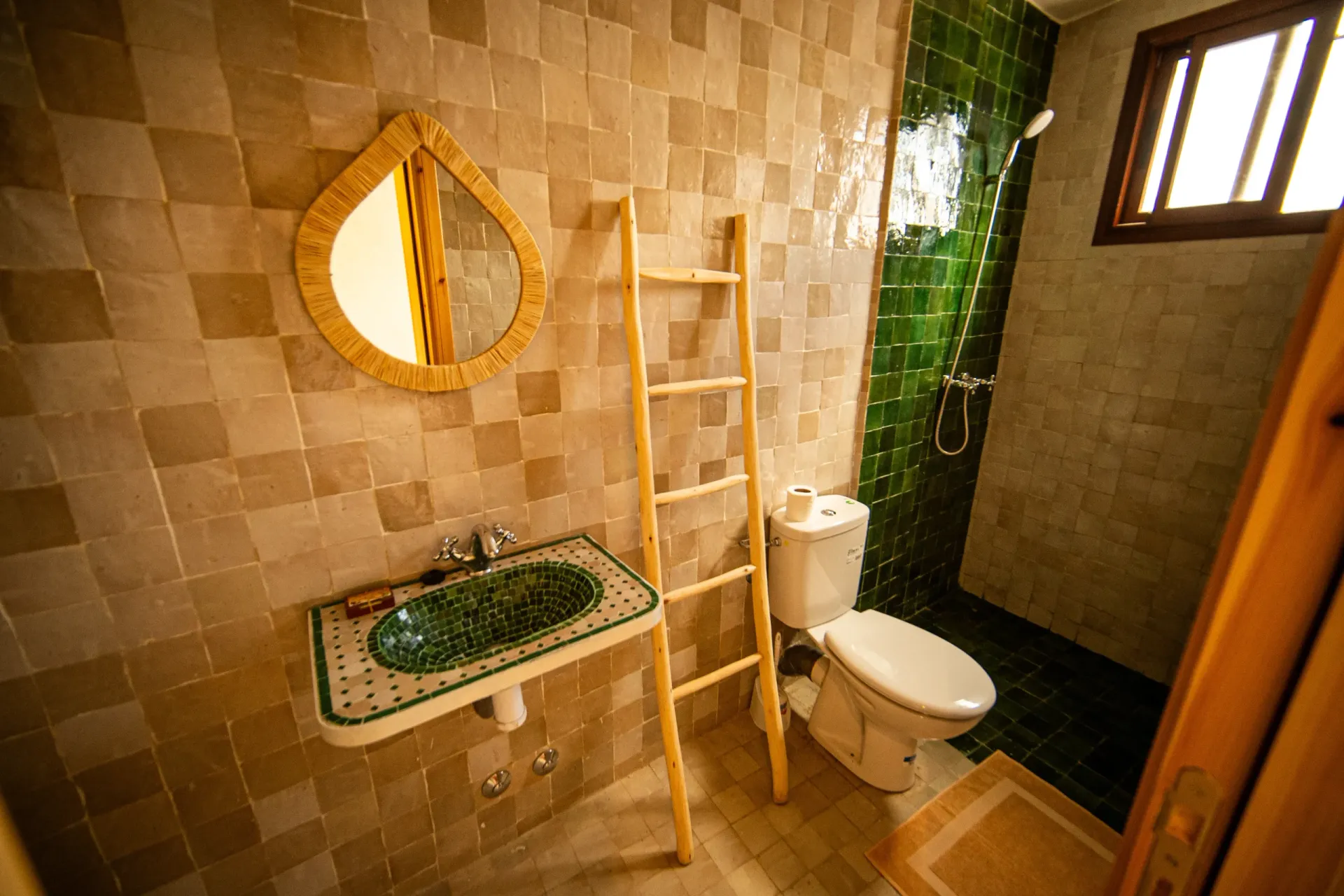 Modern bathroom with green tiles, sink, and shower in Moroccan surf camp.