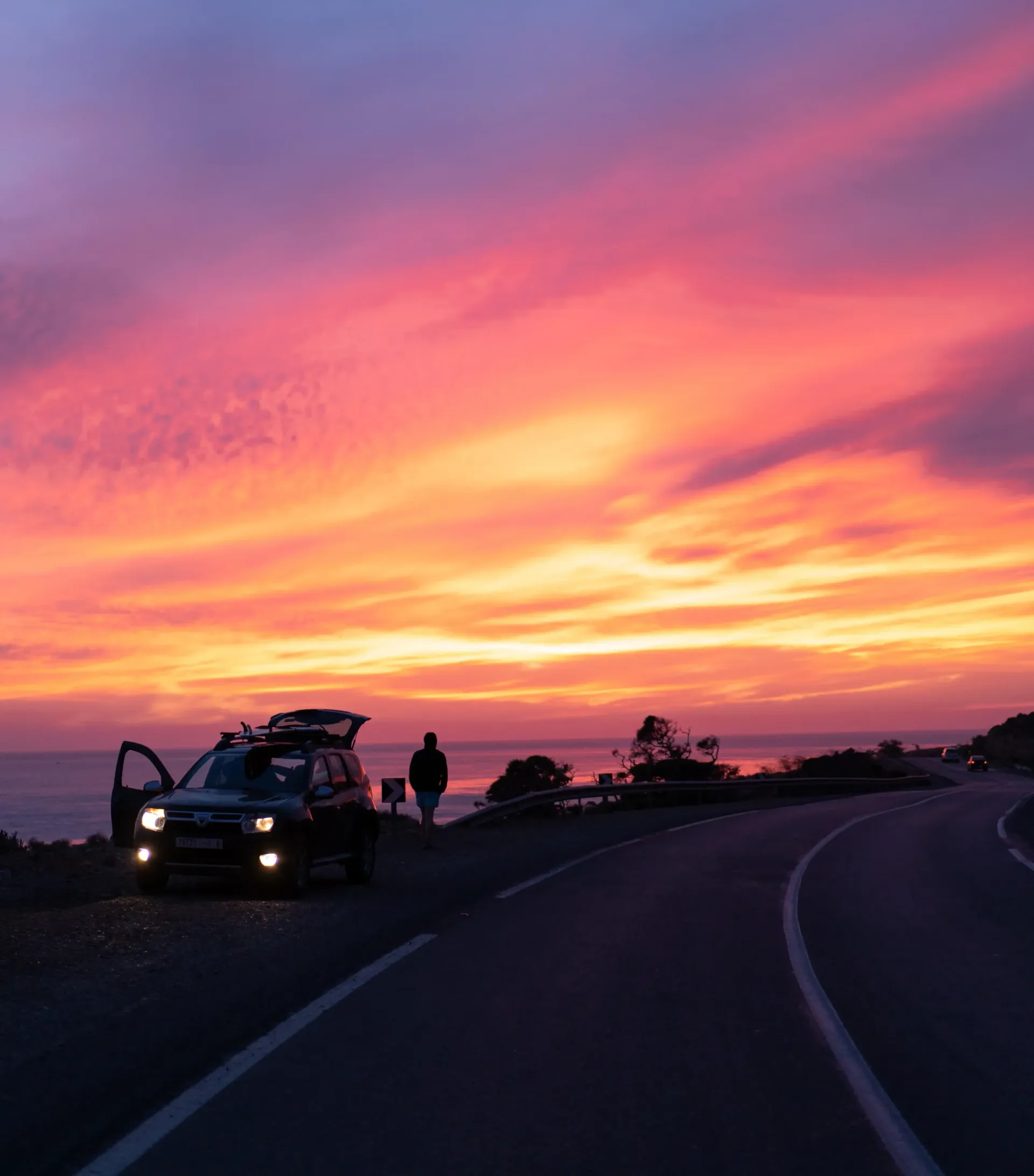 A surfer stands by a car at sunset near Imsouane, Morocco.