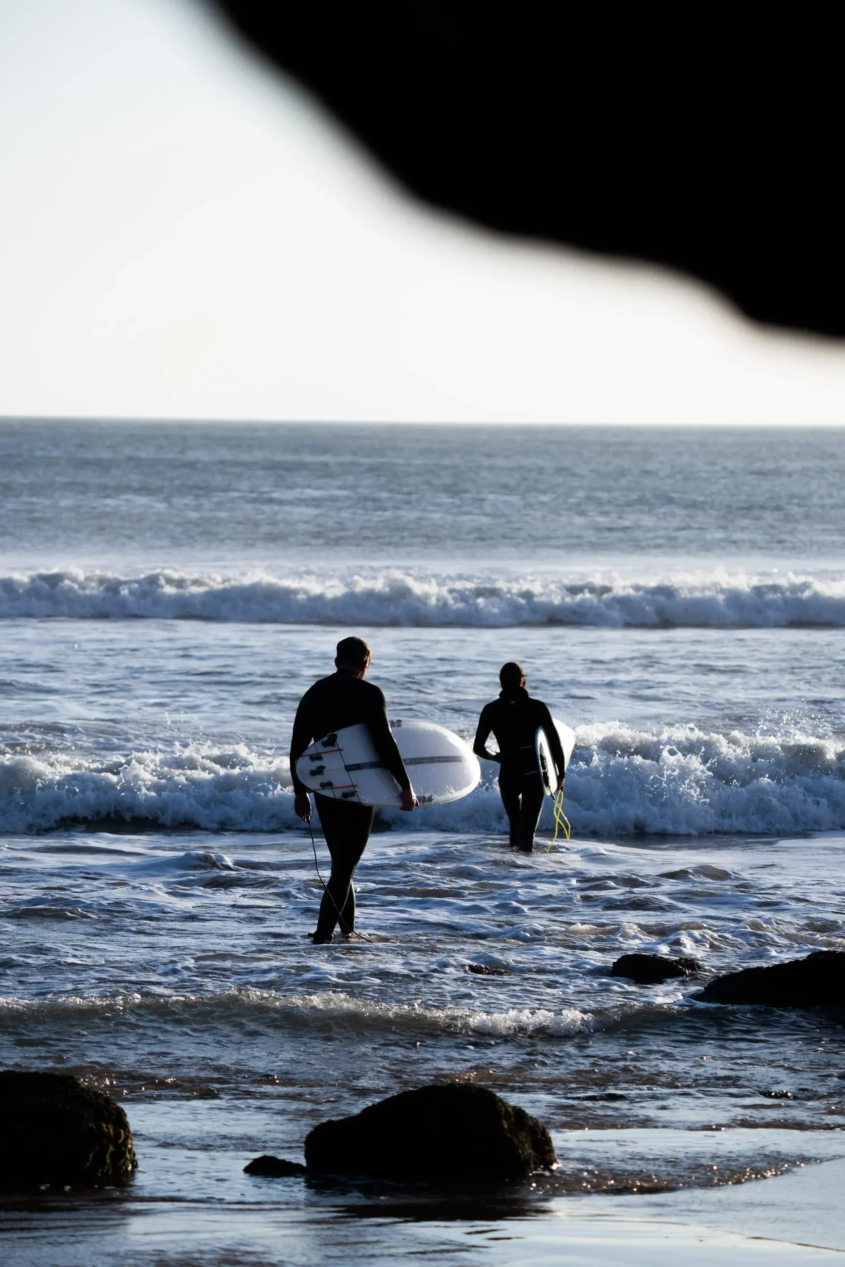 Two surfers wading into the waves at Imsouane beach, Morocco.