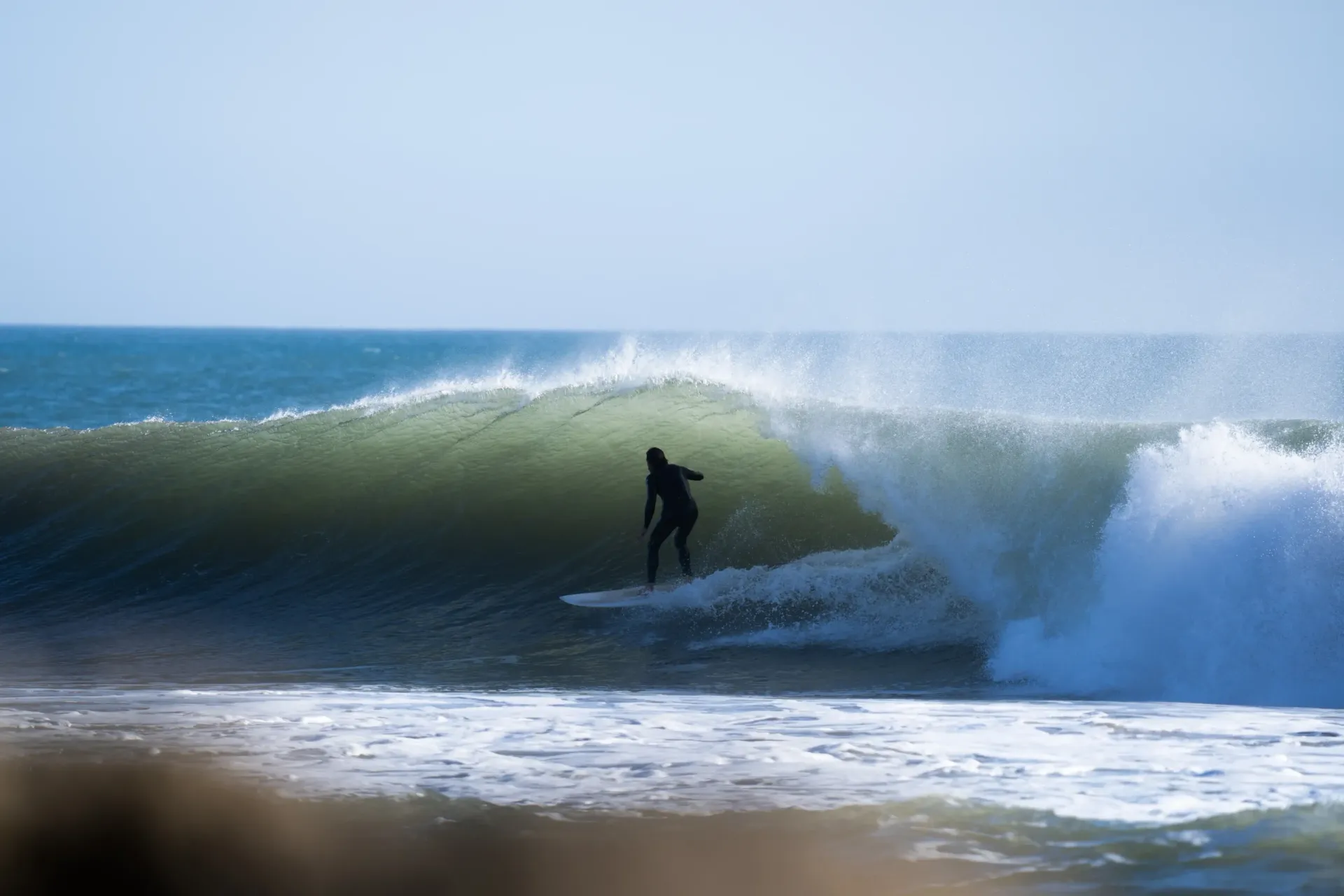 Surfer riding a large wave at Imsouane, Morocco, under a clear sky.