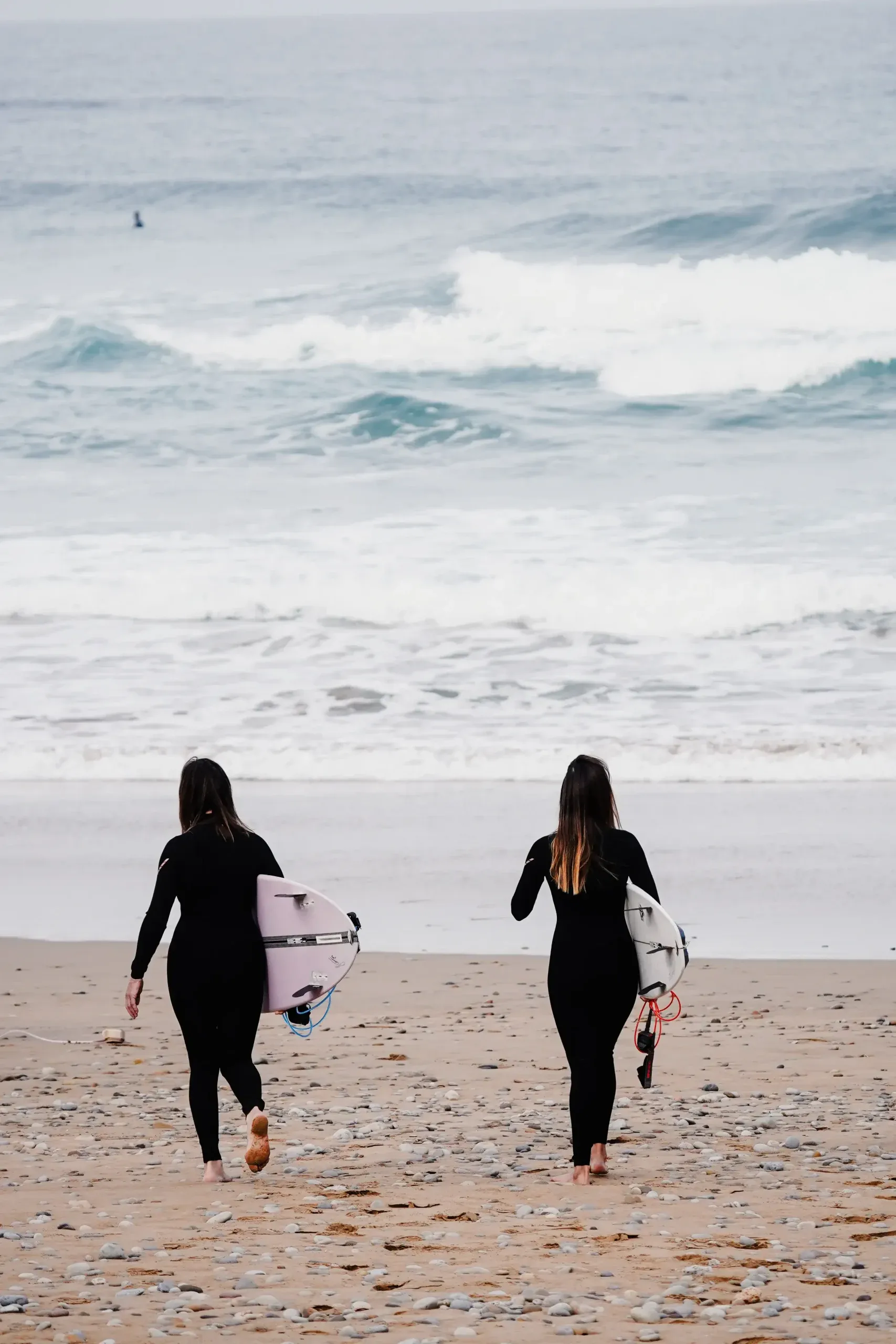 Two surfers walking on the beach towards the waves in Imsouane, Morocco.