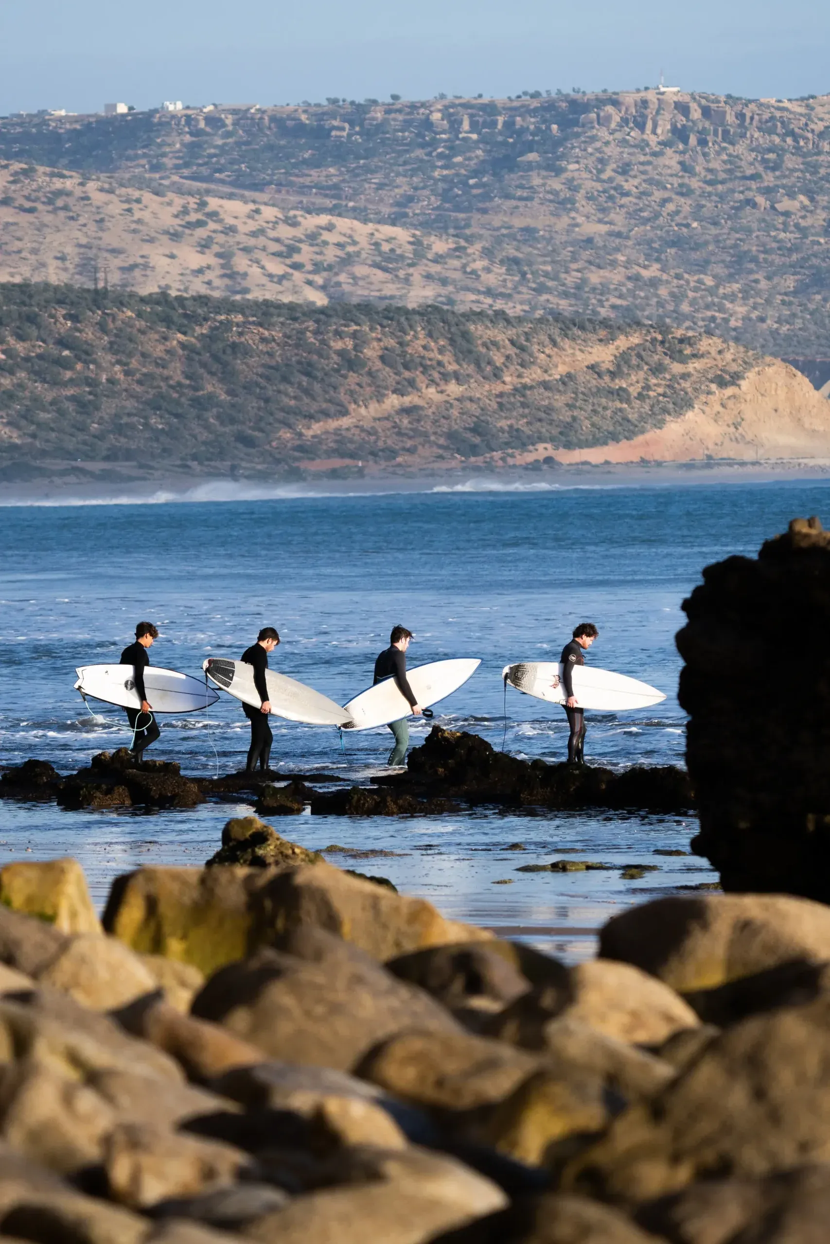 Surfers walking on rocks towards the ocean in Imsouane, Morocco.